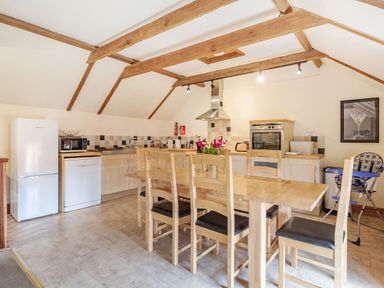 A kitchen with wooden dining table and chairs refrigerator oven and high chair at Punch Cottage in Little Glemham near Wickham Market