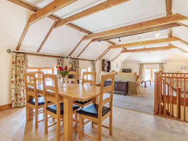 A dining area with wooden table and chairs next to a living room with sofas and wooden beams at Punch Cottage in Little Glemham near Wickham Market