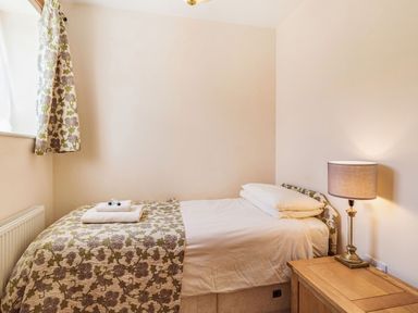 A bedroom with a single bed with floral bedspread a wooden side table with a lamp and floral curtains at Punch Cottage in Little Glemham near Wickham Market