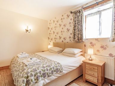 A bedroom with a double bed bedside tables lamps and floral curtains at Punch Cottage in Little Glemham near Wickham Market