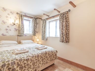 A bedroom with a double bed towels on bed floral curtains and wallpaper at Punch Cottage in Little Glemham near Wickham Market
