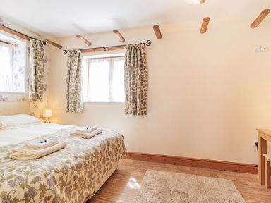 A bedroom with a bed towels on a floral bedspread two windows with floral curtains a lamp and a rug at Punch Cottage in Little Glemham near Wickham Market