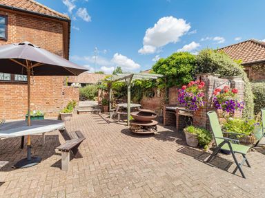 An outdoor patio area with brick walls picnic tables umbrella and garden chairs at Punch Cottage in Little Glemham near Wickham Market