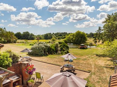 A garden with picnic tables and umbrellas near a pond with trees at Punch Cottage in Little Glemham near Wickham Market