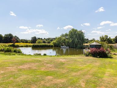 A small pond with a boat and a gazebo surrounded by grass trees and shrubs at Punch Cottage in Little Glemham near Wickham Market