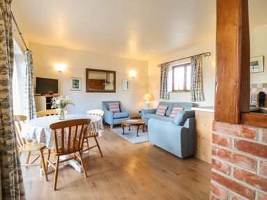 A living room with blue sofa and armchair a wooden dining table with chairs and flowers on table at Barn Owl Cottage in Little Glemham near Wickham Market