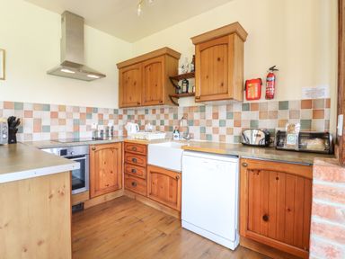 A kitchen with wooden cabinets a tiled backsplash a dishwasher an oven a toaster and a sink at Barn Owl Cottage in Little Glemham near Wickham Market