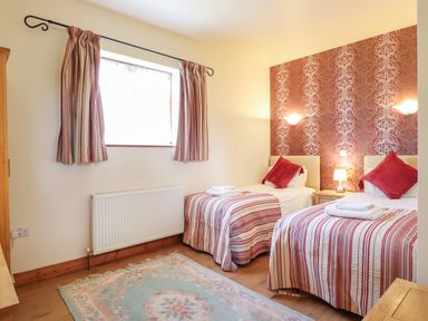 A bedroom with two single beds with striped bedding and red cushions at Barn Owl Cottage in Little Glemham near Wickham Market