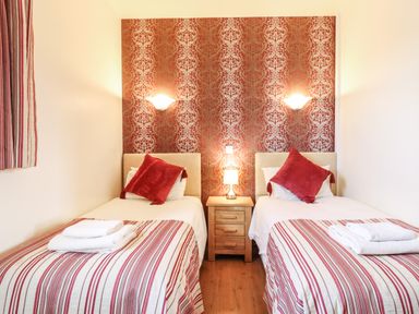A bedroom with two single beds a wooden nightstand and two wall lights at Barn Owl Cottage Little Glemham near Wickham Market