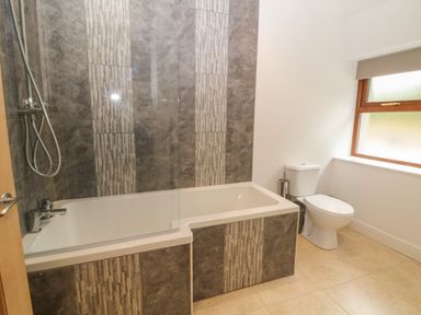 A bathroom with a bathtub and shower and a toilet near a window at Y Beudy Cottage in Clynnog Fawr