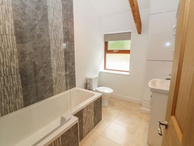 A bathroom with a bathtub shower combination a toilet a sink and a window at Y Beudy Cottage in Clynnog Fawr