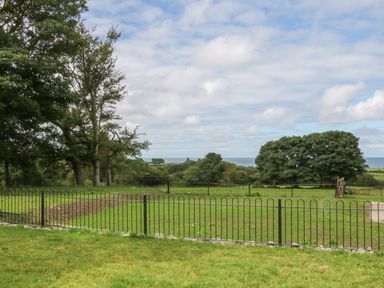 A grassy fenced yard with trees and a view of the sea at Y Beudy Cottage in Clynnog Fawr