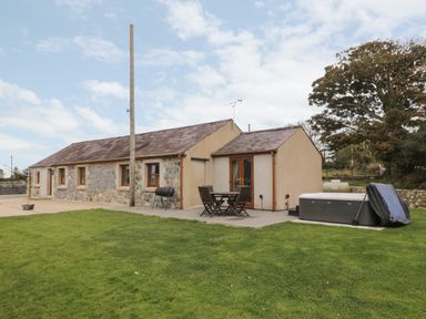 A stone and plaster house with a patio table and chairs and a hot tub on a lawn at Y Beudy Cottage in Clynnog Fawr
