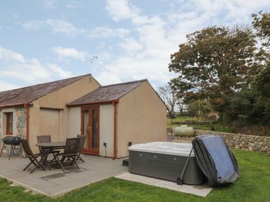 A patio area with a table and four chairs next to a hot tub outside a single story house at Y Beudy Cottage in Clynnog Fawr