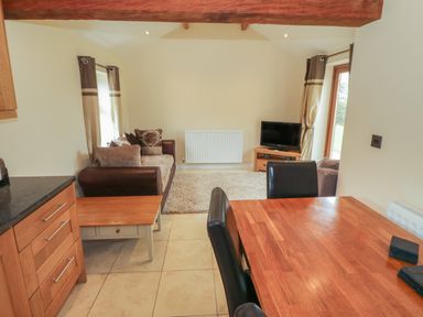 A living room and dining area with a sofa cushions television wooden table and black chairs at Y Beudy Cottage in Clynnog Fawr