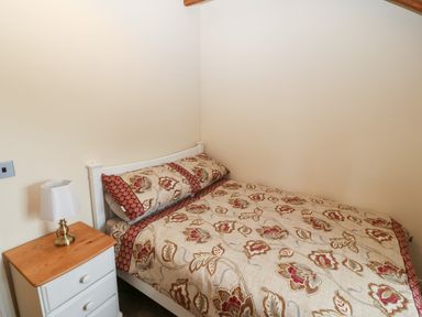 A bedroom with a bed with floral bedding and a white nightstand with a lamp at Y Beudy Cottage in Clynnog Fawr