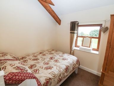 A bedroom with a bed covered with floral bedding a window with a mirror on the sill and a wooden wardrobe at Y Beudy Cottage in Clynnog Fawr