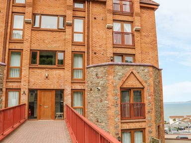 The entrance to a brick and stone apartment building with a red railing pathway and a view of the sea in the background at 37 Ocean Park in Westward Ho