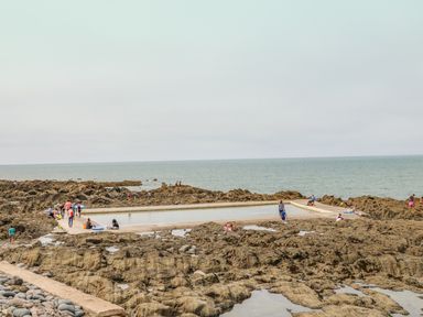 A rocky seaside area with a rectangular tidal pool and people around it at 37 Ocean Park in Westward Ho
