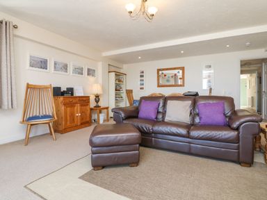 A living room with a brown leather sofa and ottoman wooden chairs a wooden cabinet and bookshelf at 37 Ocean Park in Westward Ho