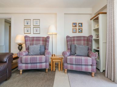 Two plaid armchairs with gray pillows between two wooden side tables and lamps in a living room at 37 Ocean Park in Westward Ho