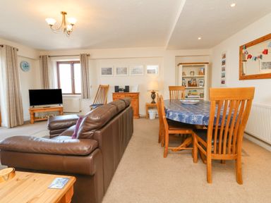 A living room with a brown leather sofa wooden dining table and chairs a television on a stand and shelves at 37 Ocean Park in Westward Ho