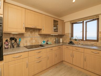 A kitchen with wooden cabinets a stove a sink and an open window overlooking the sea at 37 Ocean Park Westward Ho