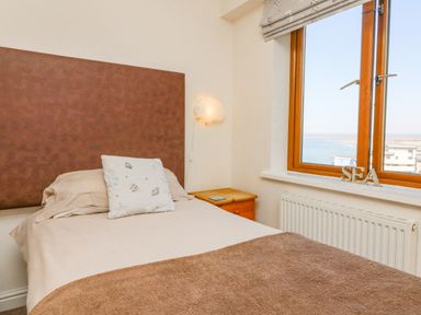 A bedroom with a single bed next to a wooden bedside table and a window showing a sea view at 37 Ocean Park in Westward Ho