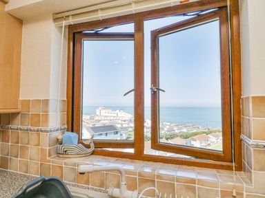 A kitchen window with beige tiled walls and a white faucet overlooking houses and the sea at 37 Ocean Park in Westward Ho