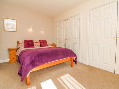 A bedroom with a wooden bed with purple bedding and pillows bedside tables and white closets at 37 Ocean Park in Westward Ho