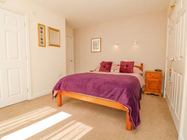 A bedroom with a double bed covered with purple bedding and wooden bedside cabinet at 37 Ocean Park in Westward Ho