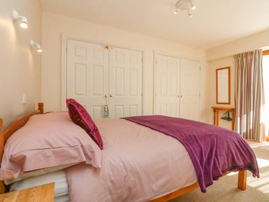 A bedroom with a double bed with purple bedding two sets of double doors and a wall mirror at 37 Ocean Park in Westward Ho