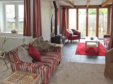 A living room with striped sofas red chair coffee table and large windows at Hour Cottage in Stow-on-the-Wold