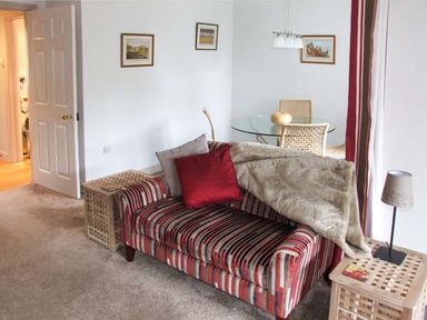 A living room with a striped sofa with cushions and a throw a glass dining table with chairs and framed pictures on the wall at Hour Cottage in Stow-on-the-Wold