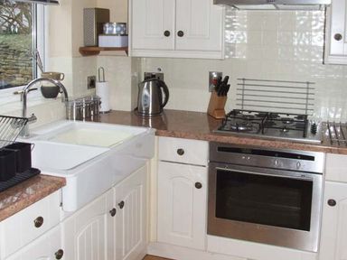 A kitchen with a white sink a stainless steel kettle a knife block a gas stove and an oven at Hour Cottage in Stow-on-the-Wold