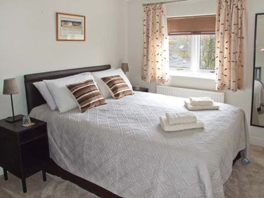 A bedroom with a bed with white bedding and striped pillows beside a window with curtains at Hour Cottage in Stow-on-the-Wold