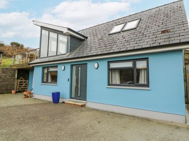 A blue house exterior with dark roof windows and a front door with planters outside at Ty Henri in Tresaith