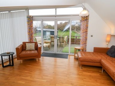 A living room with leather armchairs a side table and sliding glass doors leading to a wooden deck at Ty Henri in Tresaith