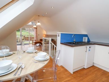 A kitchen and dining area with a round table set for four and a living room with glass doors leading outside at Ty Henri in Tresaith