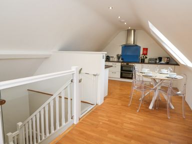 A kitchen and dining area with a round table set for four and transparent chairs near a staircase with a safety gate at Ty Henri in Tresaith
