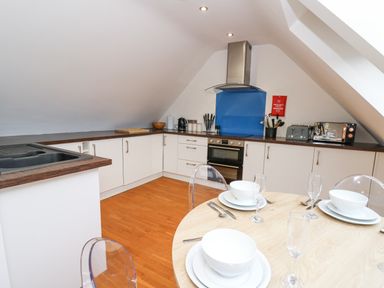 A kitchen with white cabinets wooden countertops a blue backsplash and a table set with white dishes and glasses at Ty Henri in Tresaith