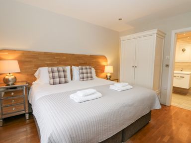 A bedroom with a large bed two bedside tables with lamps a white wardrobe and an open door to a bathroom at Ty Henri in Tresaith
