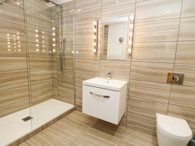 A bathroom with a glass shower, floating sink cabinet, mirror with lights, and a toilet at Ty Henri in Tresaith