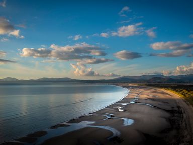 A beach with water and mountains in the background at Murmur Y Don Harlech