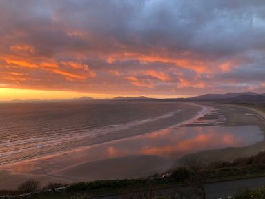 A beach with sunset colors reflecting on the water at Murmur Y Don in Harlech