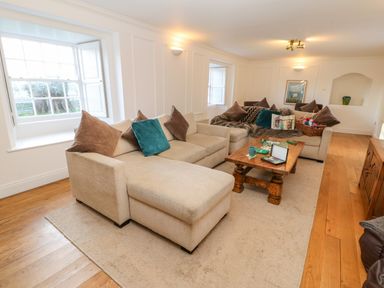 A sitting room with beige sofas, wooden coffee table, cushions, and windows at East Farm House in Humshaugh near Hexham