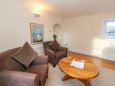 A sitting area with two brown armchairs a wooden coffee table with a magazine a framed picture of a sheep on the wall and a window with a radiator at East Farm House in Humshaugh near Hexham