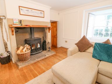 A living room with a wood burning stove firewood baskets a beige sofa with cushions and a window at East Farm House Humshaugh near Hexham