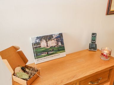 A wooden dresser with an open box containing leaves and a small bottle a book a cordless phone and a candle at East Farm House in Humshaugh near Hexham