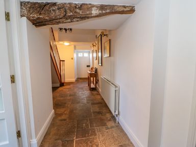 A hallway with stone floor a staircase on the left and a wooden table under pictures at East Farm House Humshaugh near Hexham